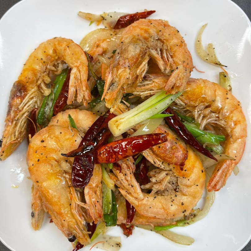 Salt and pepper shrimp with dried red chilies, green onions, and white onions on a white plate.