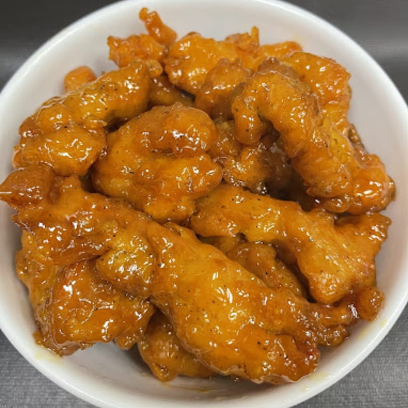 A white bowl filled with Mr You Chinese Food's orange chicken, glistening with sauce and black pepper.